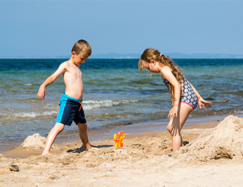 Zwei Kinder spielen am Strand im Sand mit dem Meer im Hintergrund